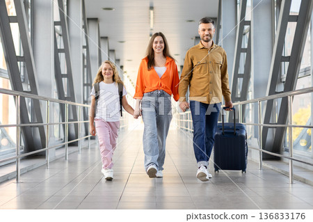Smiling caucasian family walking through airport terminal with luggage, holding hands Smiling caucasian family walking through airport terminal with luggage, holding hands 136833176
