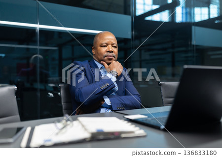 Thoughtful mature black businessman looking at laptop screen in office Thoughtful mature black businessman looking at laptop screen in office 136833180