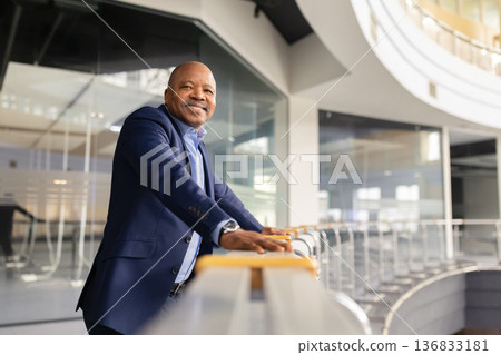 Mature black businessman leaning on balcony railing in office building and smiling Mature black businessman leaning on balcony railing in office building and smiling 136833181