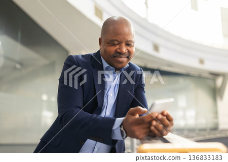 Thoughtful mature black businessman looking at smartphone in office atrium Thoughtful mature black businessman looking at smartphone in office atrium 136833183