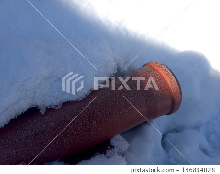 Red Sewer Pipe Covered in Snow on a Winter Day in an Outdoor Setting 136834028