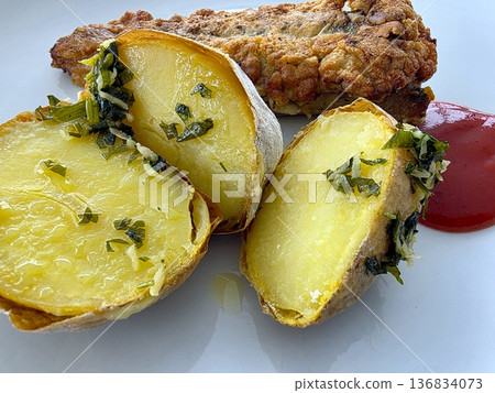 Baked Potatoes and Fried Fish Served on a White Plate With Sauce 136834073