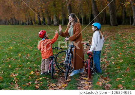 Mother high fives kids with bicycles in sunny autumn park 136834681