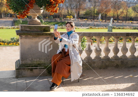 Smiling woman taking smartphone selfie in sunny autumn European garden Smiling woman taking smartphone selfie in sunny autumn European garden 136834692