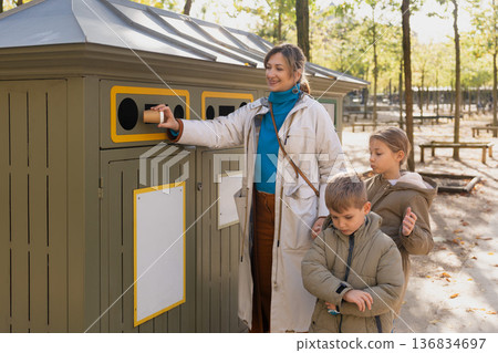 Mother teaching kids recycling paper at park eco station outdoors 136834697