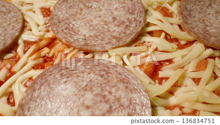 Preparing a pizza with cheese and salami at a kitchen counter in the evening hours 136834751