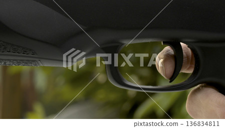 Person prepares to pull trigger on firearm in an outdoor setting during daylight hours Person prepares to pull trigger on firearm in an outdoor setting during daylight hours 136834811