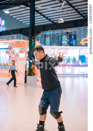Man balancing on rollerblades at a brightly lit indoor rink Man balancing on rollerblades at a brightly lit indoor rink 136834897
