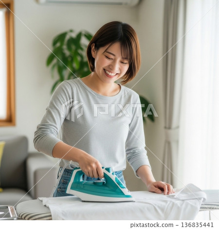 年輕女子正在客廳的熨衣板上熨衣服 136835441