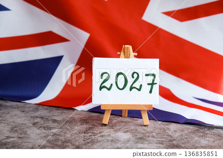 Paper note with text 2027 on National symbol of Great Britain. British wave the UK silky flag background. Financial outlook planning, new year annual report Paper note with text 2027 on National symbol of Great Britain. British wave the UK silky flag background. Financial outlook planning, new year annual report 136835851