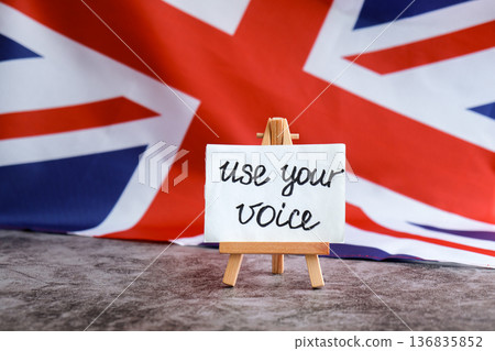 Paper note with words USE YOUR VOICE on National symbol of Great Britain. British wave the UK silky flag background. Ellection political participation campaign and civic engagement Paper note with words USE YOUR VOICE on National symbol of Great Britain. British wave the UK silky flag background. Ellection political participation campaign and civic engagement 136835852