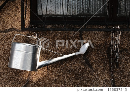 Afternoon sunlight. The contrast between the tin watering can hanging on the wall and the deep shadow. Vintage texture. Afternoon sunlight. The contrast between the tin watering can hanging on the wall and the deep shadow. Vintage texture. 136837243