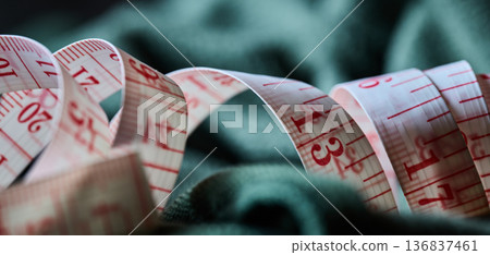 Close up of a white and red measuring tape resting on dark green textile material 136837461
