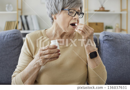 Senior woman taking pill dose for disease therapy, sitting on sofa at home Senior woman taking pill dose for disease therapy, sitting on sofa at home 136837631