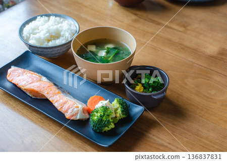 A breakfast of grilled salmon, miso soup, rice, and natto on a brightly lit dining table 136837831