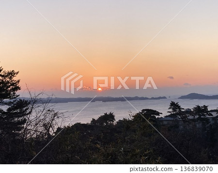 A quiet dawn scene in which the sun rises from behind the islands floating in the sea, softly coloring the sky and the surface of the sea. 136839070