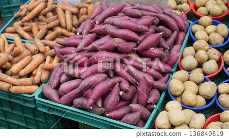 Carrots, sweet potatoes and potatoes in plastic boxes in front of a vegetable store Carrots, sweet potatoes and potatoes in plastic boxes in front of a vegetable store 136840819