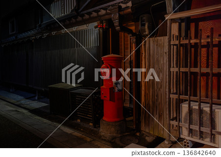 A red round postbox standing in an old townscape at night. Traditional Japanese scenery. Retro postbox. A red round postbox standing in an old townscape at night. Traditional Japanese scenery. Retro postbox. 136842640