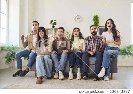 Excited friends watching TV at home as football fans cheering together on couch Excited friends watching TV at home as football fans cheering together on couch 136843827