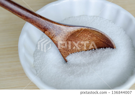 Wooden spoon partially submerged in salt inside white dish illustrating cooking ingredient and salt reduction awareness campaign. Wooden spoon partially submerged in salt inside white dish illustrating cooking ingredient and salt reduction awareness campaign. 136844007