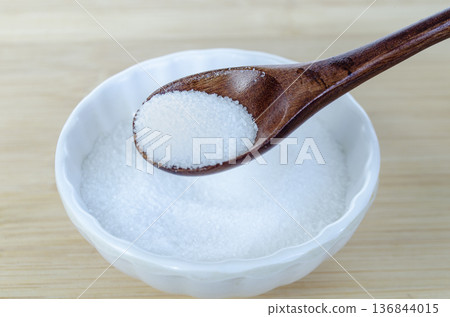 White sugar in spoon resting on ceramic dish representing daily sweet consumption and blood sugar management concept. White sugar in spoon resting on ceramic dish representing daily sweet consumption and blood sugar management concept. 136844015