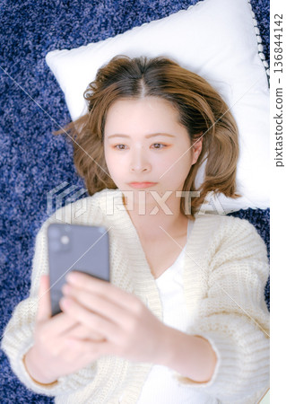 一位二十多歲的日本女性在家中拿著智慧型手機 一位二十多歲的日本女性在家中拿著智慧型手機 136844142