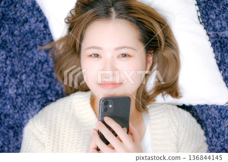 A Japanese woman in her twenties holding a smartphone at home 136844145