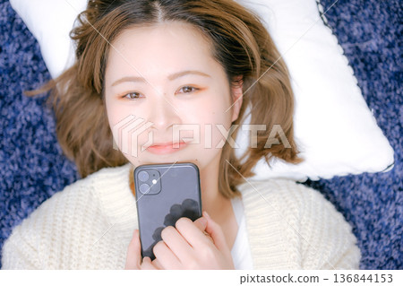 A Japanese woman in her twenties holding a smartphone at home 136844153