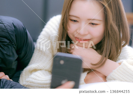 一位二十多歲的日本女性在家中看著她的智慧型手機 136844255