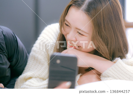 一位二十多歲的日本女性在家中看著她的智慧型手機 136844257