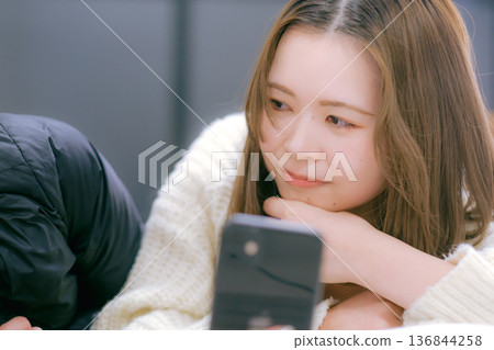 一位二十多歲的日本女性在家中看著她的智慧型手機 136844258