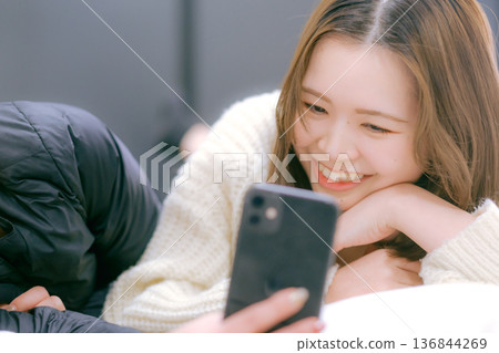 一位二十多歲的日本女性在家中看著她的智慧型手機 136844269