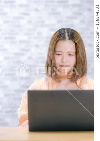 一位二十多歲的日本女子看著筆記型電腦，顯得非常擔憂。 136844331