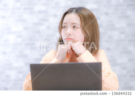 一位二十多歲的日本女子看著筆記型電腦，顯得非常擔憂。 136844332