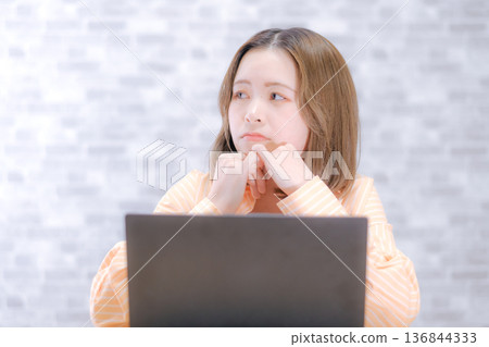 一位二十多歲的日本女子看著筆記型電腦,顯得非常擔憂。 一位二十多歲的日本女子看著筆記型電腦,顯得非常擔憂。 136844333