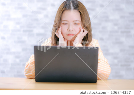 一位二十多歲的日本女子看著筆記型電腦,顯得非常擔憂。 一位二十多歲的日本女子看著筆記型電腦,顯得非常擔憂。 136844337