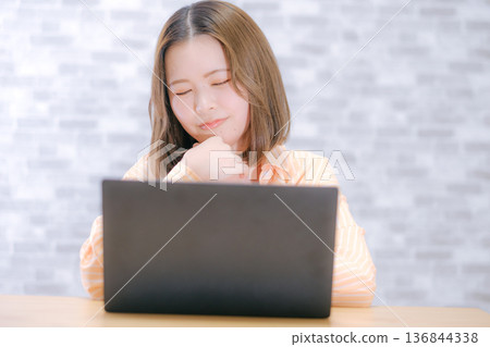 A Japanese woman in her twenties worried while looking at a laptop computer 136844338