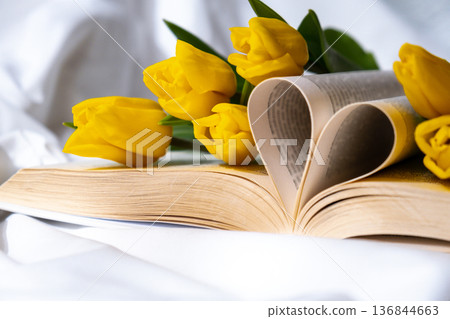 Book pages in shape of heart symbol love with bouquet of pink tulips on messy bed. Romantic morning scene. Greeting card Holiday flowers springtime Book pages in shape of heart symbol love with bouquet of pink tulips on messy bed. Romantic morning scene. Greeting card Holiday flowers springtime 136844663