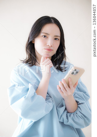 一名女子正在操作智慧型手機,搜尋線上服務等,她低頭看著手機,神情焦慮不安,一手托著下巴。 一名女子正在操作智慧型手機,搜尋線上服務等,她低頭看著手機,神情焦慮不安,一手托著下巴。 136844857