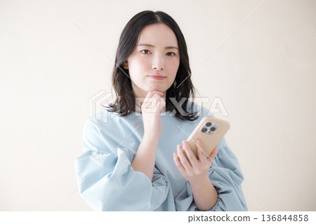 一名女子正在操作智慧型手機,搜尋線上服務等,她低頭看著手機,神情焦慮不安,一手托著下巴。 一名女子正在操作智慧型手機,搜尋線上服務等,她低頭看著手機,神情焦慮不安,一手托著下巴。 136844858