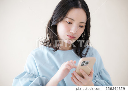 一名女子正在操作智慧型手機,搜尋線上服務等,她低頭看著手機,神情焦慮不安,一手托著下巴。 一名女子正在操作智慧型手機,搜尋線上服務等,她低頭看著手機,神情焦慮不安,一手托著下巴。 136844859