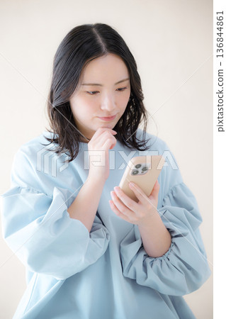 A woman operating a smartphone. Searching for online services, etc., looking at her smartphone, worried and troubled, with her hand on her chin. A woman operating a smartphone. Searching for online services, etc., looking at her smartphone, worried and troubled, with her hand on her chin. 136844861