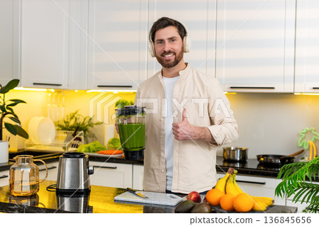 Middle-aged man blending banana smoothie in home kitchen listening to music on headphones for diet 136845656