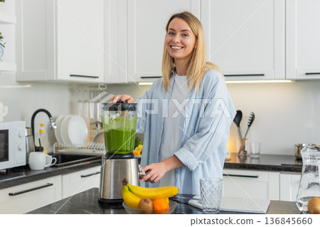 Young woman blending fresh smoothie with apple banana spinach spirulina in home kitchen for morning 136845660