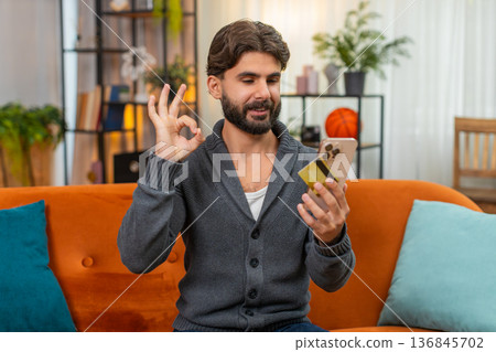 Indian man confirms online purchase with smartphone and card enters cvv nods relief approval gesture Indian man confirms online purchase with smartphone and card enters cvv nods relief approval gesture 136845702