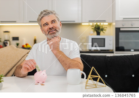 Middle-aged man puts money cash coins in piggy bank saving budget promise savings dollar discipline 136845765