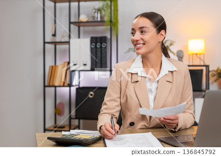 Young businesswoman totals month on calculator checks receipts and invoices nods with satisfaction Young businesswoman totals month on calculator checks receipts and invoices nods with satisfaction 136845792