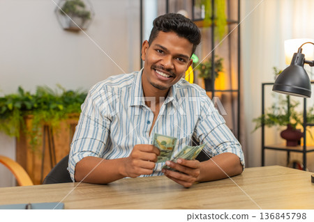 Indian man counts dollar cash after salary bonus plans invest smiles at earnings profit wealth joy 136845798