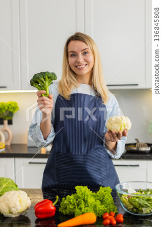 Young woman showing broccoli and cauliflower in kitchen promoting keto diet healthy grocery shopping 136845808