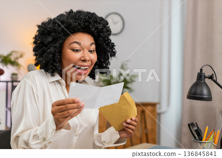 African American businesswoman reads letter smiles happy at good news job approval big salary raise African American businesswoman reads letter smiles happy at good news job approval big salary raise 136845841